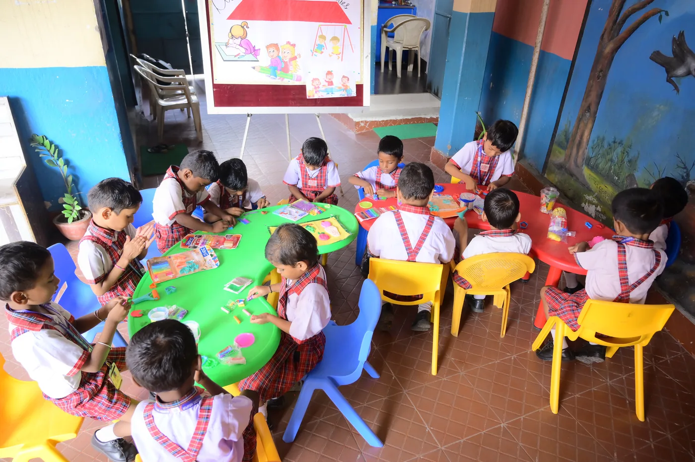 Children working together at activity tables with their teacher’s chart behind them