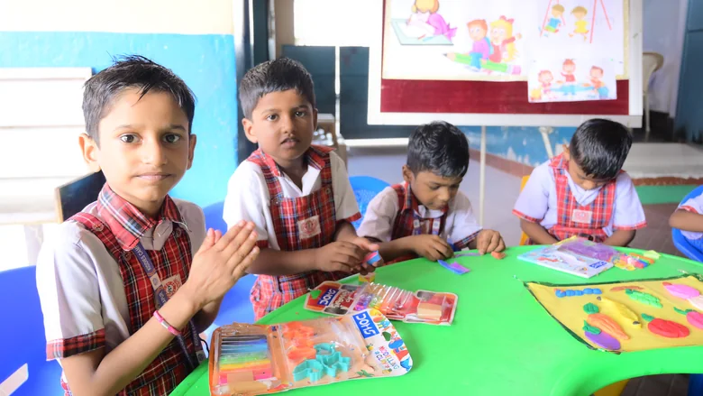 Children at a green activity table with clay and craft kits, the class chart behind them